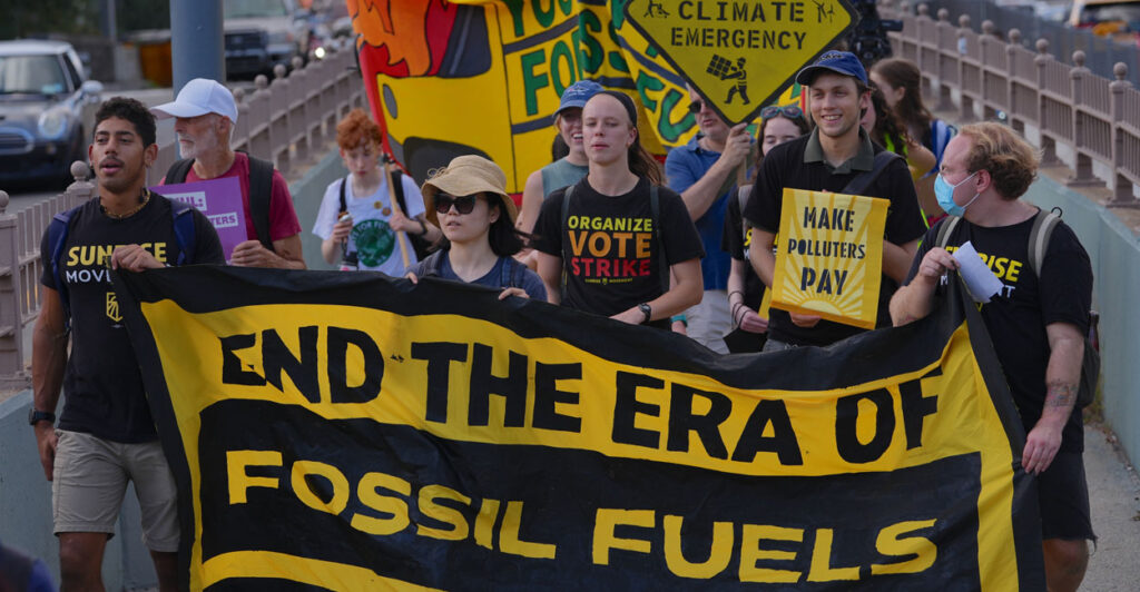 young climate activists marching and holding a banner that says end the era of fossil fuels