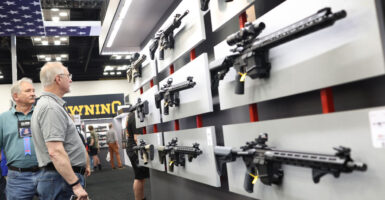 gun manufacturing Expo attendees look at several models of AR-15s displayed on a wall