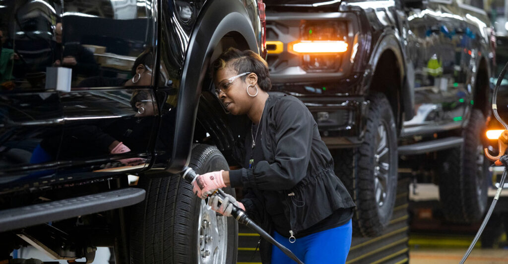 a black woman working on black pickup trucks in a Ford production line