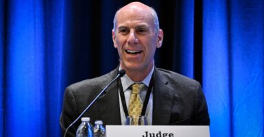 James Boasberg smiles as he sits down at a table in front of a microphone.