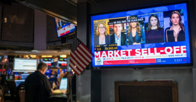 A picture of the stock exchange with a large screen TV in front with The graphic market selloff and several commentators on screen