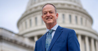 Rep. Mark Messmer in a blue suit and tie stands outdoors in front of the Capitol with the dome in the background.