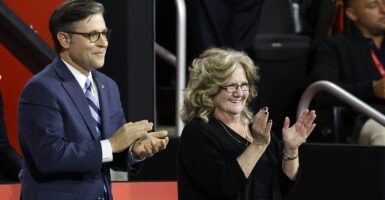 Bev Vance stands and applauds with a smile on her face as Mike Johnson stands to her right.