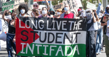masked students protest in favor of Palestine on the streets with a banner that says long live the student intifada