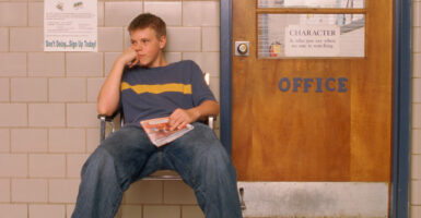 Teen boy slouching in a chair in a hallway outside the principal's office.