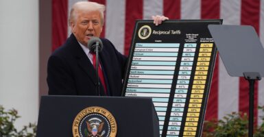 Donald Trump stands behind a podium and holds up a chart with tariff information during a press conference.