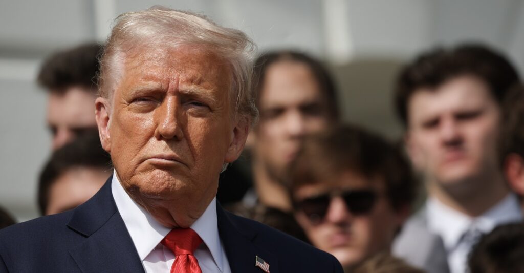 Donald Trump stands at a press conference and looks straight ahead.