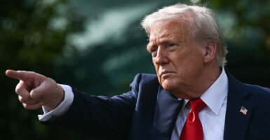 Donald Trump in a blue suit and red tie with a raised arm pointing in the distance