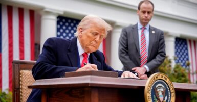 Donald Trump sits at a desk slightly bent over as he signs an executive order.