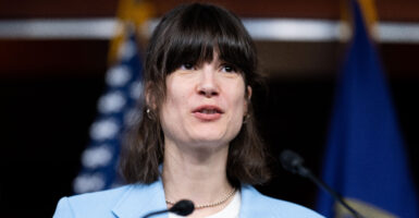 Rep. Marie Gluesenkamp Perez In a light blue suit jacket stands at a microphone with an American flag in the background