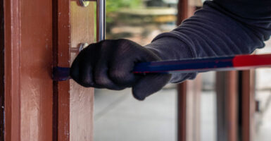 Close up of goved arm, with crowbar breaking into house.