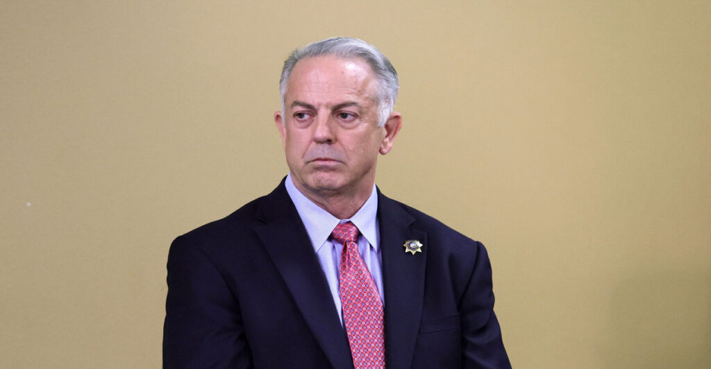 Then Clark County Sheriff Joe Lombardo looks to his left against a tan backdrop.