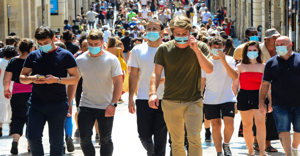 During COVID, a mass of people stroll down a street in Bordeaux, France, all in masks.