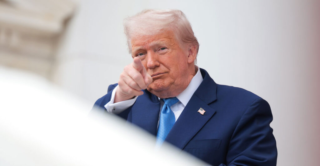 A grinning President Donald Trump points toward camera.