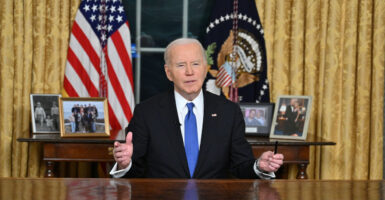 President Joe Biden, hands spread, behind the Resolute Desk in Oval Office delivering his Farewell Address.
