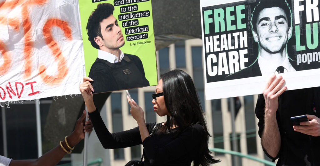 Black woman in profile holding a sign quoting Luigi Mangione at a pro-Mangione rally.