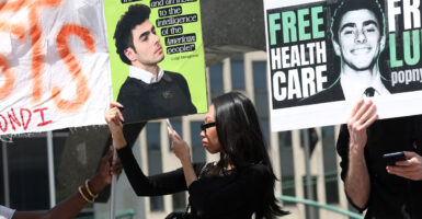 Black woman in profile holding a sign quoting Luigi Mangione at a pro-Mangione rally.