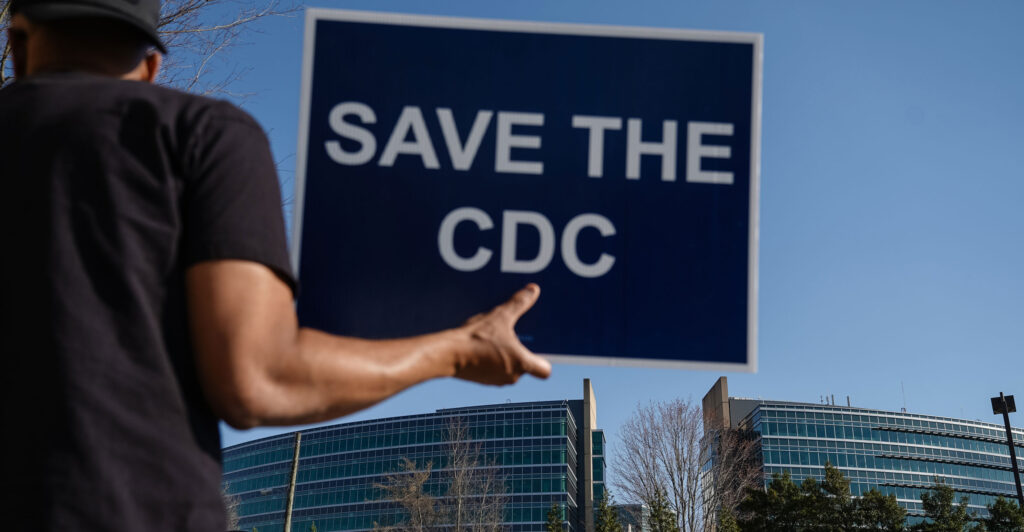 People protesting personnel cuts at the Centers for Disease Control hold signs outside the organization's Atlanta, Georgia, headquarters on March 12.