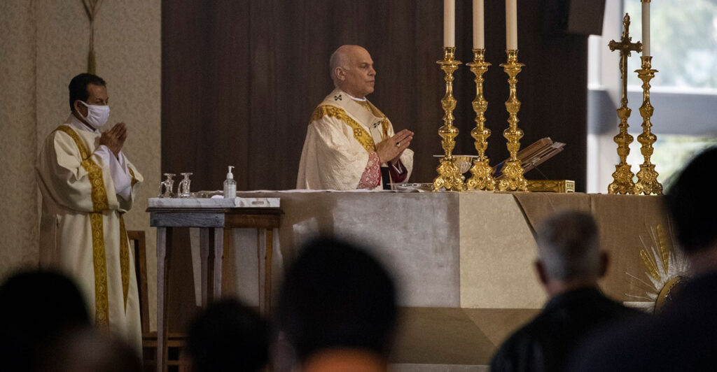 Archbishop Salvatore Cordileone stands in front of an altar with his hands clasped together as he speaks during an in-church Easter Mass celebration.