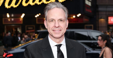 Jake Tapper poses outdoors for a photo while wearing a suit.