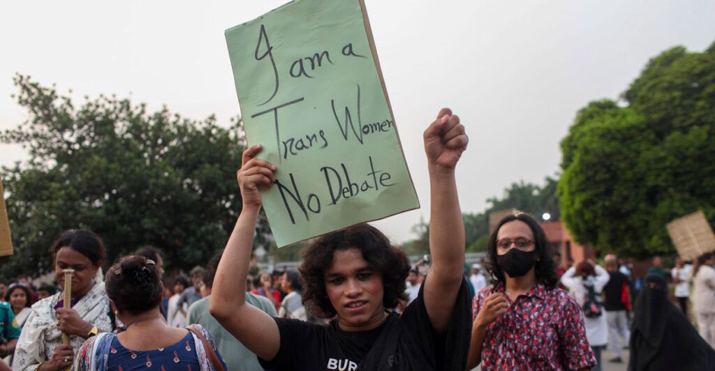 A person holds up a green sign that says, "I am a trans women. No debate."