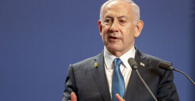 Israeli Prime Minister Benjamin Netanyahu, wearing a suite and blue tie, speaks into a microphone.