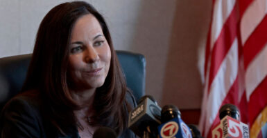 Leah Foley sits at the bench with a slight smile on her face while many microphones are before her.