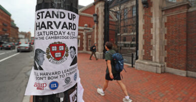 A "Stand Up Harvard" flier on a pole at Harvard University, as a male walks past.