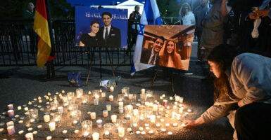 Lit candles are placed on the ground in front of two portraits of the victims of a anti-Israel shooting.