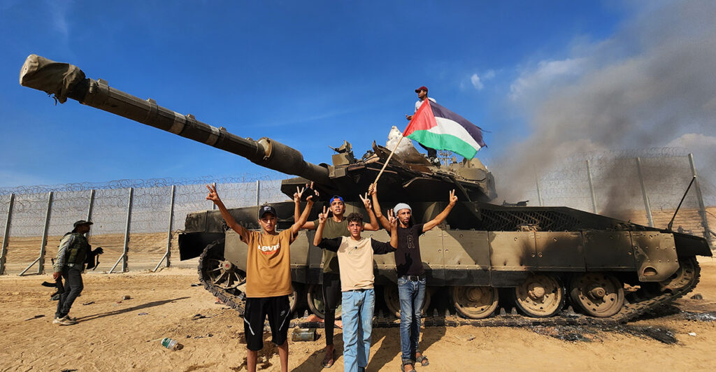 Hamas terrorists unfurl a Palestinian flag as they destroy an Israeli tank in Gaza City, Gaza, on Oct. 7, 2023.