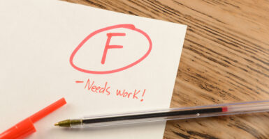 The corner of a white school paper with a circled F and "Needs Work!" written in red.