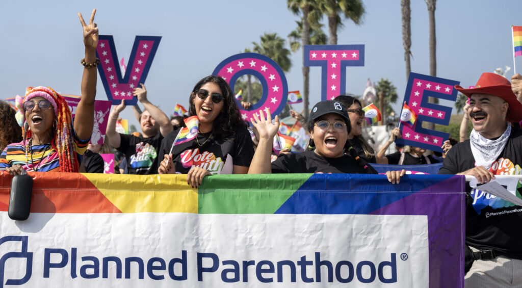 Three women and a male carry a Planned Parenthood banner ringed in rainbow colors during the Orange County Pride Parade in 2024.
