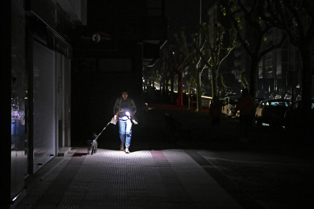 A woman walking her dog lights her way down the street with a cellphone amid a blackout in Spain.