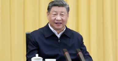 A smiling Chinese Chairman Xi in dark blue jacket in front of gold curtains.