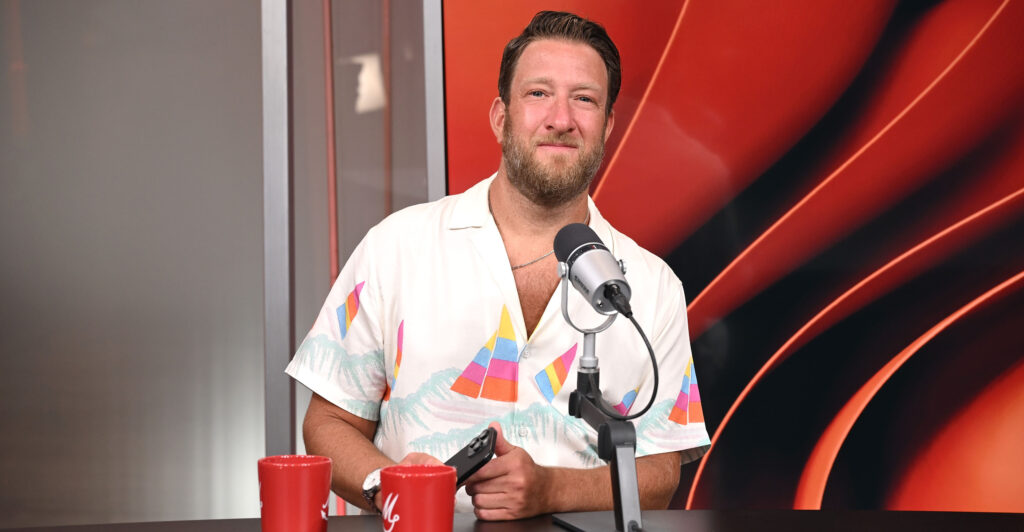 Dave Portnoy wears a white party shirt as he sits in front of a microphone.