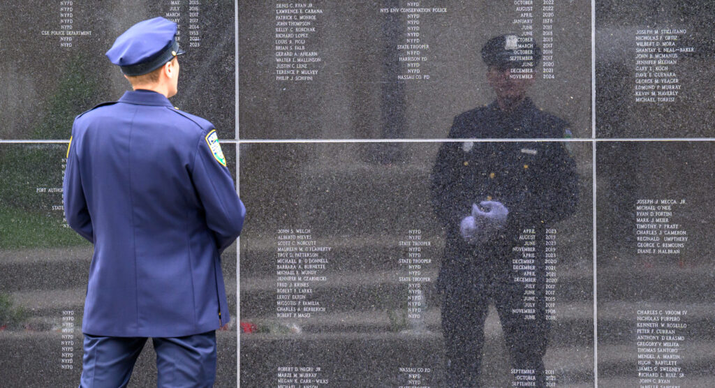 Riverhead, NY, Police Officer Bill Krause stands in front of the black wall etched with the names of New York officers who have lost their lives. Officer Krause's reflection is seen in the wall.