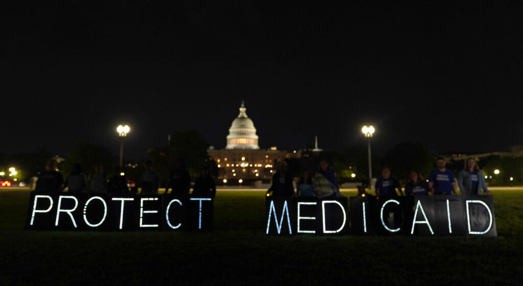 White lights spelling out "Protect Medicaid" are lit in front of the U.S. Capitol at nighttime.