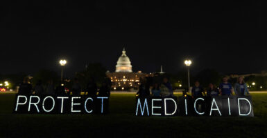 White lights spelling out "Protect Medicaid" are lit in front of the U.S. Capitol at nighttime.