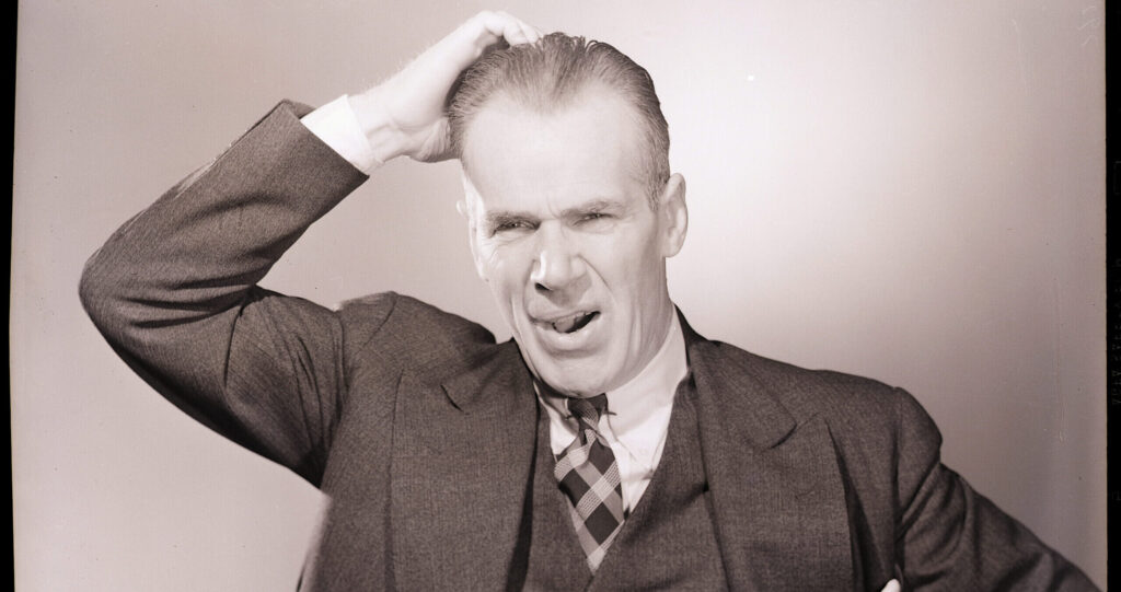 Man in a suit scratches his head quizzically in an old black and white photograph