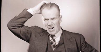 Man in a suit scratches his head quizzically in an old black and white photograph