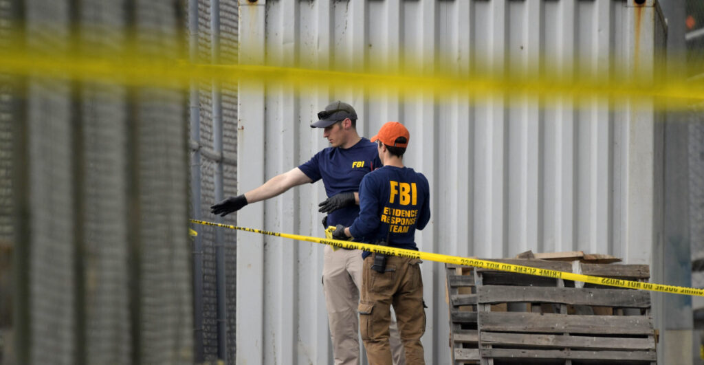 Two FBI agents examine scene of 2017 Congressional Baseball Game shooting, behind two strands of police tape