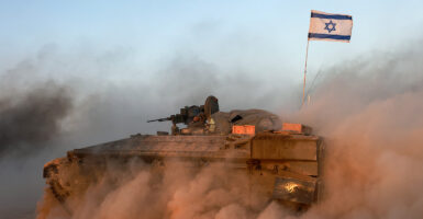An Israeli military armored vehicle with an Israeli flag on the back kicks up dust as it drives along.