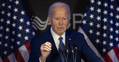 Joe Biden in a blue suit gestures in front of American flags