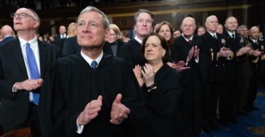 John Roberts is wearing his Supreme Court robe as he claps and looks to his right.