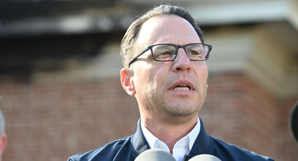 Josh Shapiro in a suit in front of a brick building.