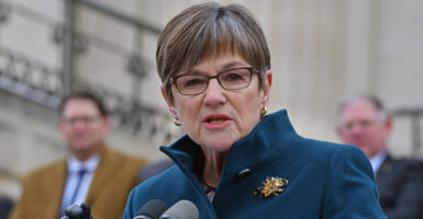 Kansas Gov. Laura Kelly in a blue winter jacket speaks at a microphone