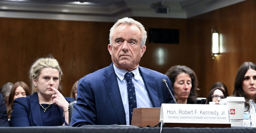 Heealth and Human Services Secretary Robert Kennedy Junior in a blue suit and blue tie sits in front of a Senate committee hearing