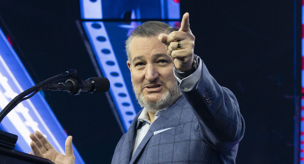 A smiling Ted Cruz in a checkered suit points.