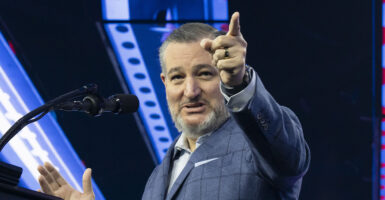 A smiling Ted Cruz in a checkered suit points.