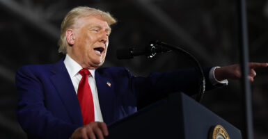 President Donald Trump in a blue suit and red tie speaks on stage at a podium